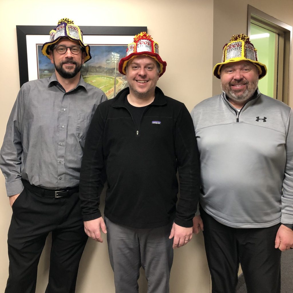 Three men wearing hats made out of a knit material with aluminum cans sewn into the hats.