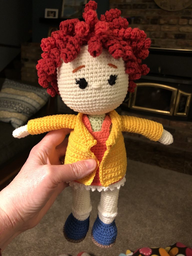 Example of crocheted doll with red curly hair and a yellow jacket.